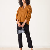 Woman wearing a mustard yellow blouse and black pants, holding a black clutch against a white background