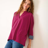 Woman wearing a magenta blouse and blue jeans against a white background