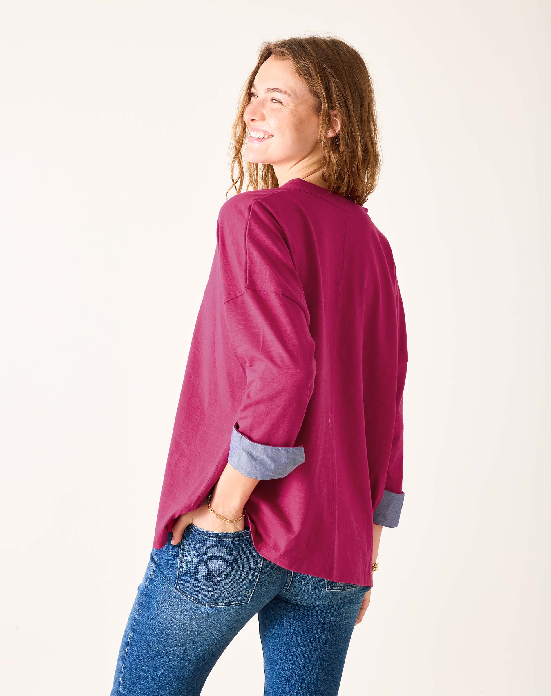 Woman wearing a magenta shirt and blue jeans on a white background