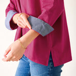 Person wearing a magenta shirt with rolled-up sleeves and blue jeans on a white background