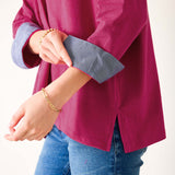 Person wearing a magenta shirt with rolled-up sleeves and blue jeans on a white background