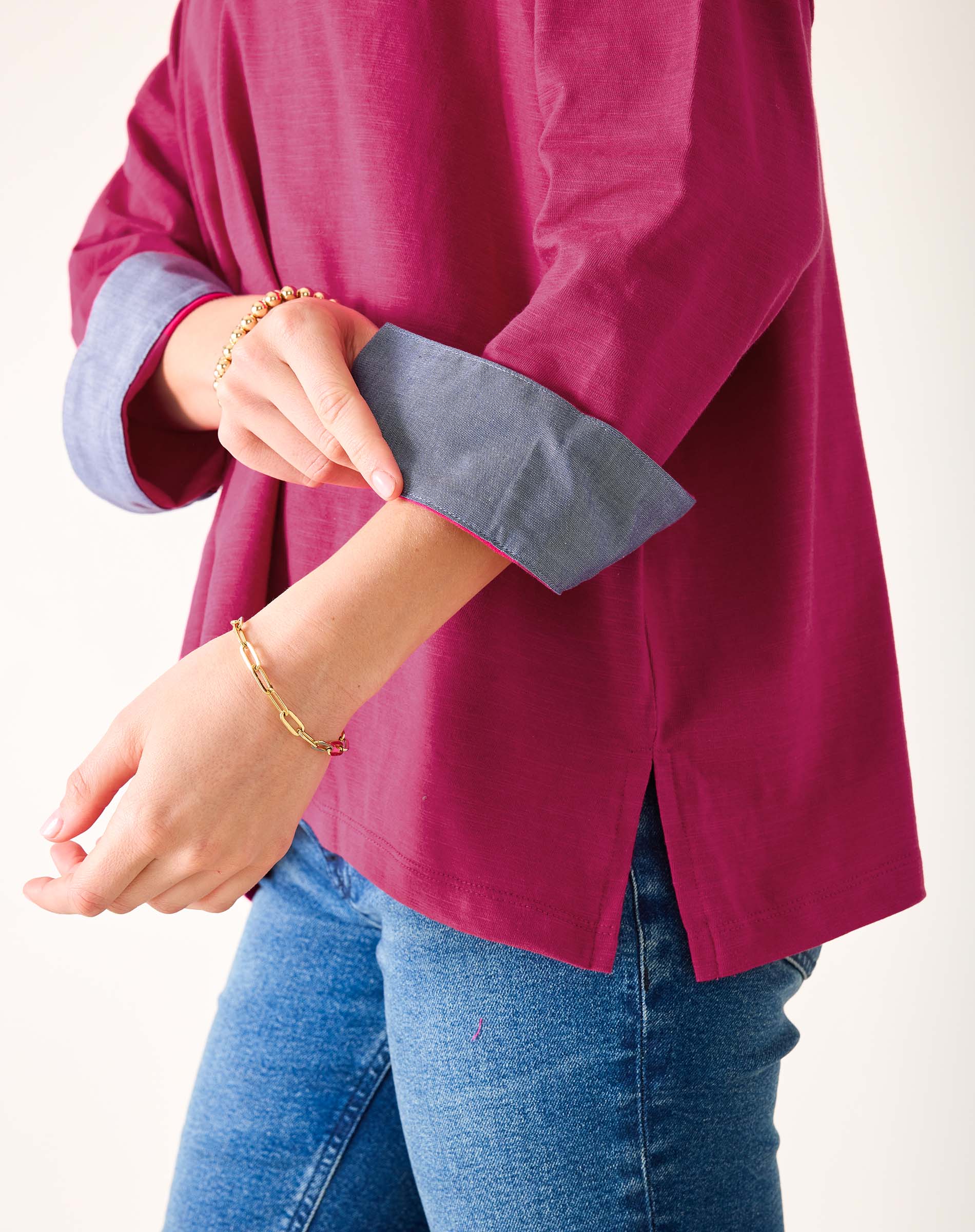 Person wearing a magenta shirt with rolled-up sleeves and blue jeans on a white background