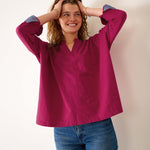 Woman wearing a magenta blouse with blue cuffs and trim, standing against a plain background
