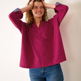 Woman wearing a magenta blouse with blue cuffs and trim, standing against a plain background