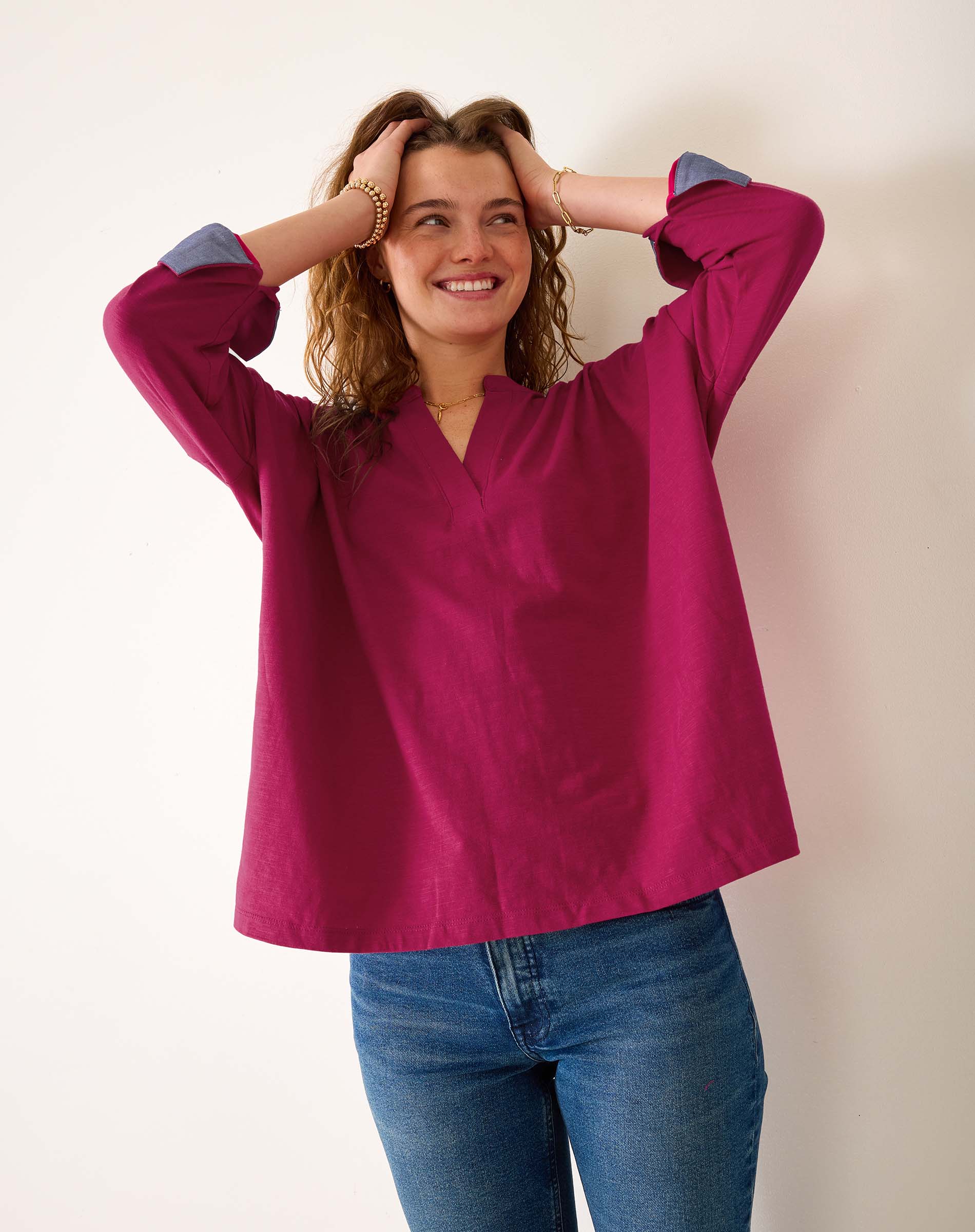 Woman wearing a magenta blouse with blue cuffs and trim, standing against a plain background