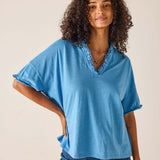 Woman wearing a blue top with ruffled neckline against a beige background