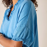 Person wearing a blue blouse with ruffled neckline on a plain background