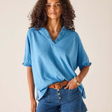 Woman wearing a blue shirt and denim shorts against a beige background