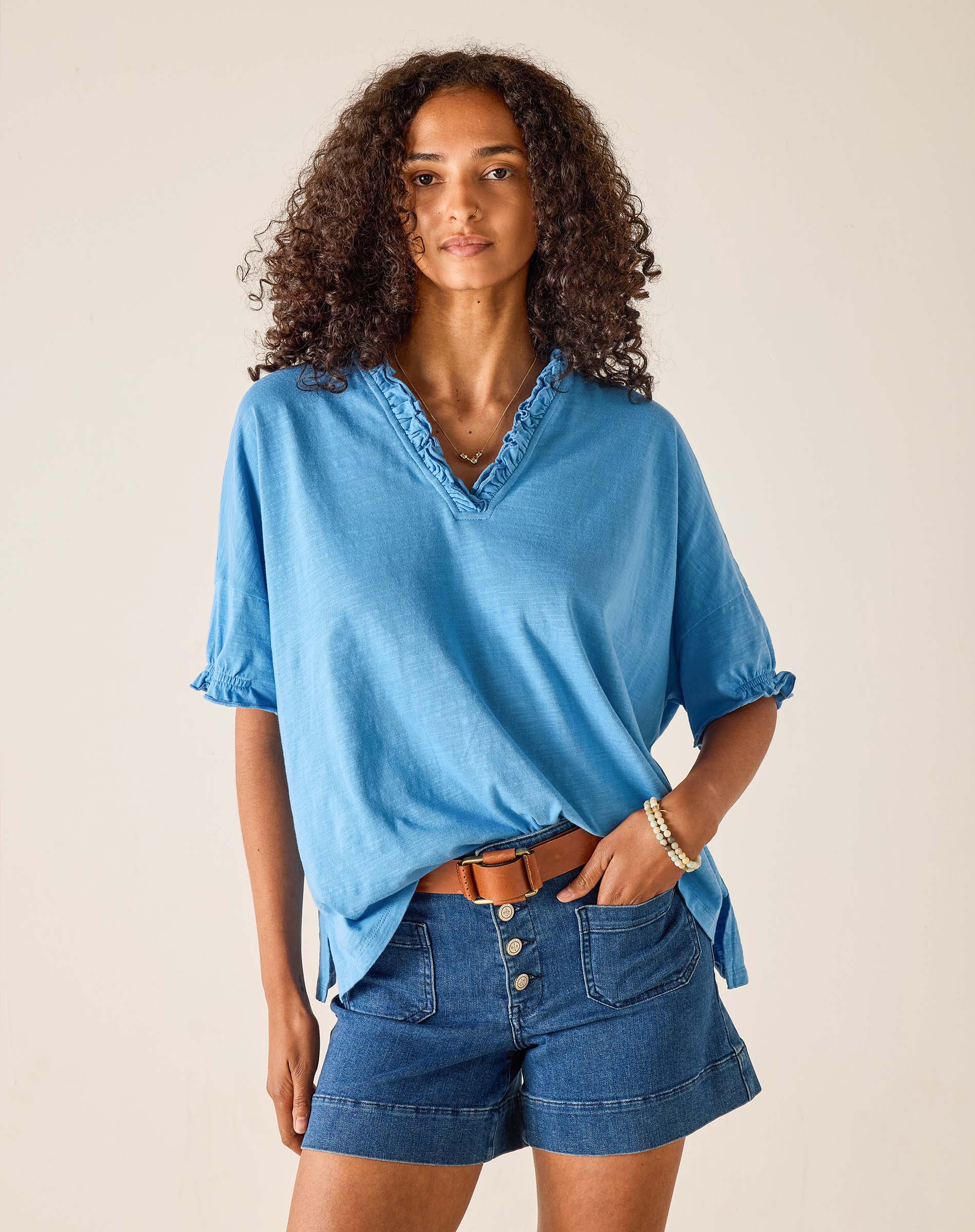 Woman wearing a blue shirt and denim shorts against a beige background