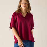 Woman wearing a burgundy blouse with ruffled neckline and blue jeans on a plain background