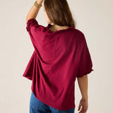 Person wearing a burgundy top and blue jeans against a beige background