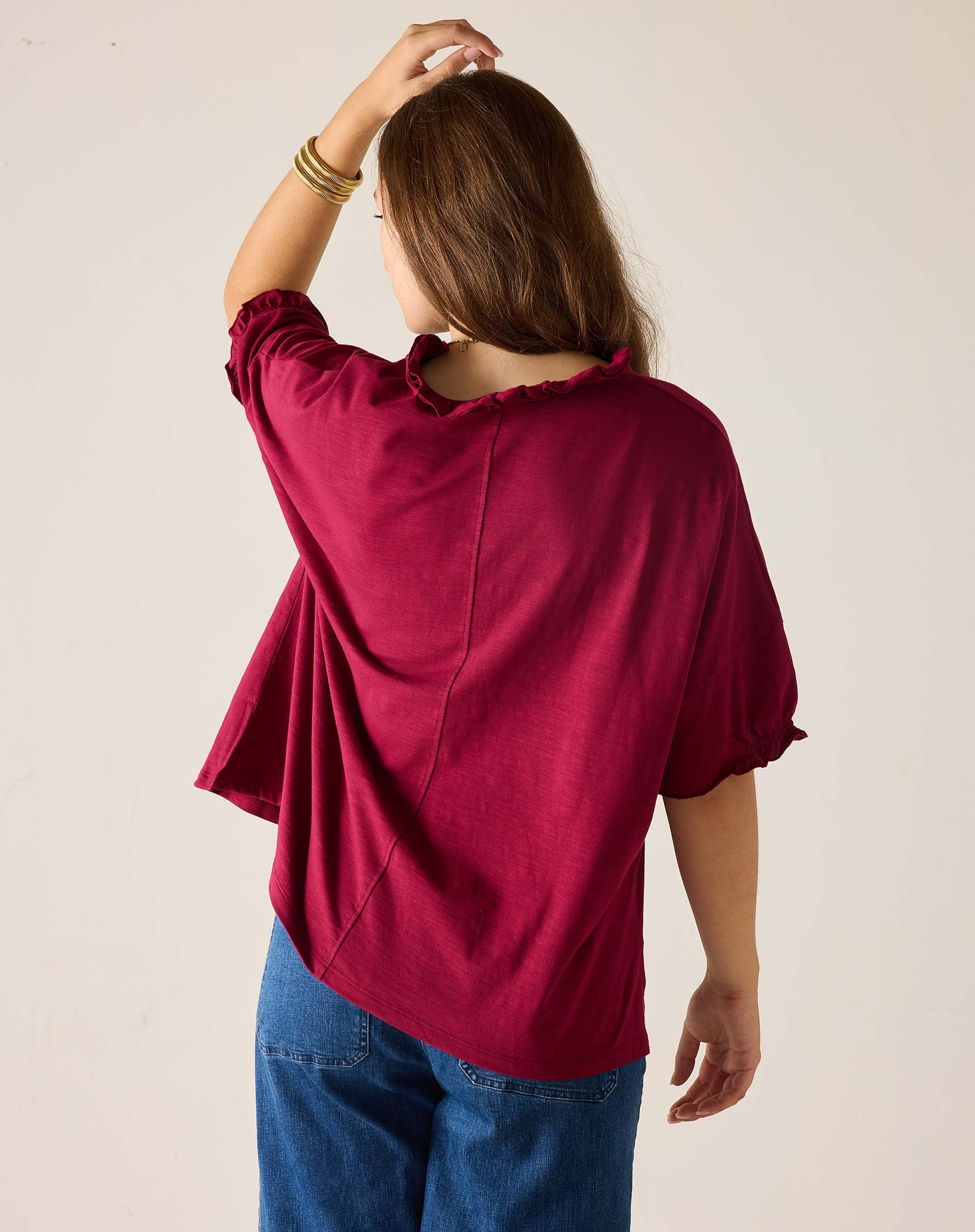 Person wearing a burgundy top and blue jeans against a beige background