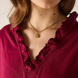 Close-up of a person wearing a gold necklace with a pendant, against a neutral background.