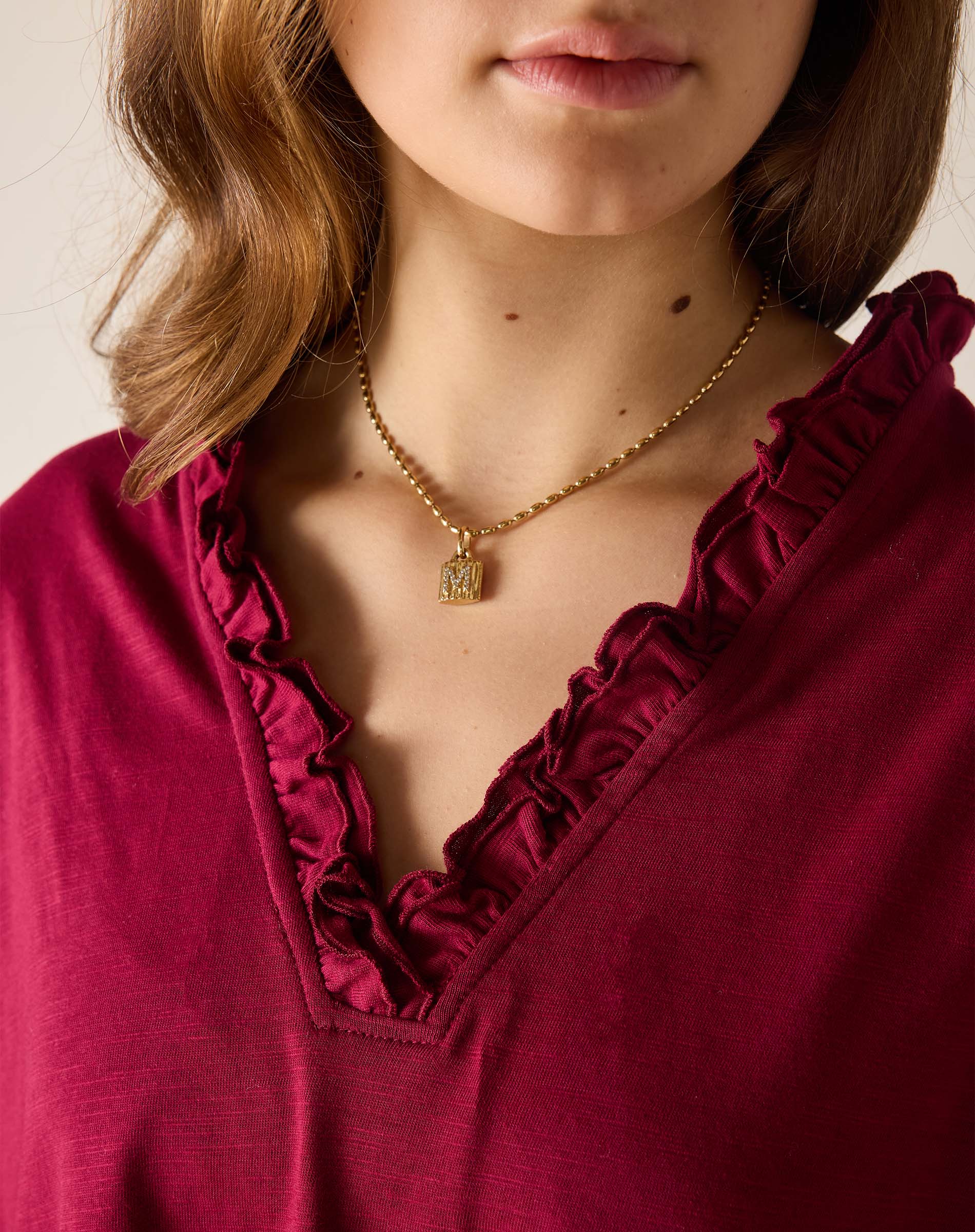 Close-up of a person wearing a gold necklace with a pendant, against a neutral background.
