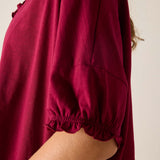 Close-up of a burgundy dress with ruffled neckline and balloon sleeves on a neutral background
