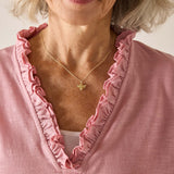 Woman wearing a pink blouse with ruffled collar and a gold necklace with a butterfly pendant.