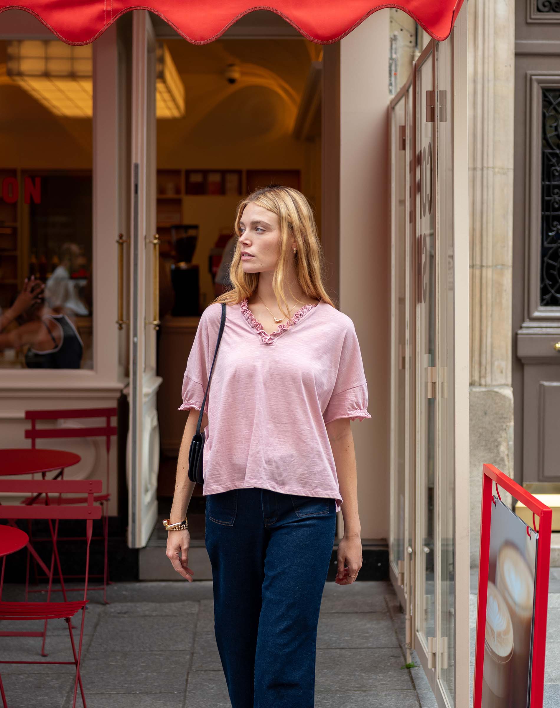 Woman walking past a cafe with red awning and chairs