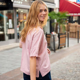 Woman in a pink shirt standing on a street with shops in the background