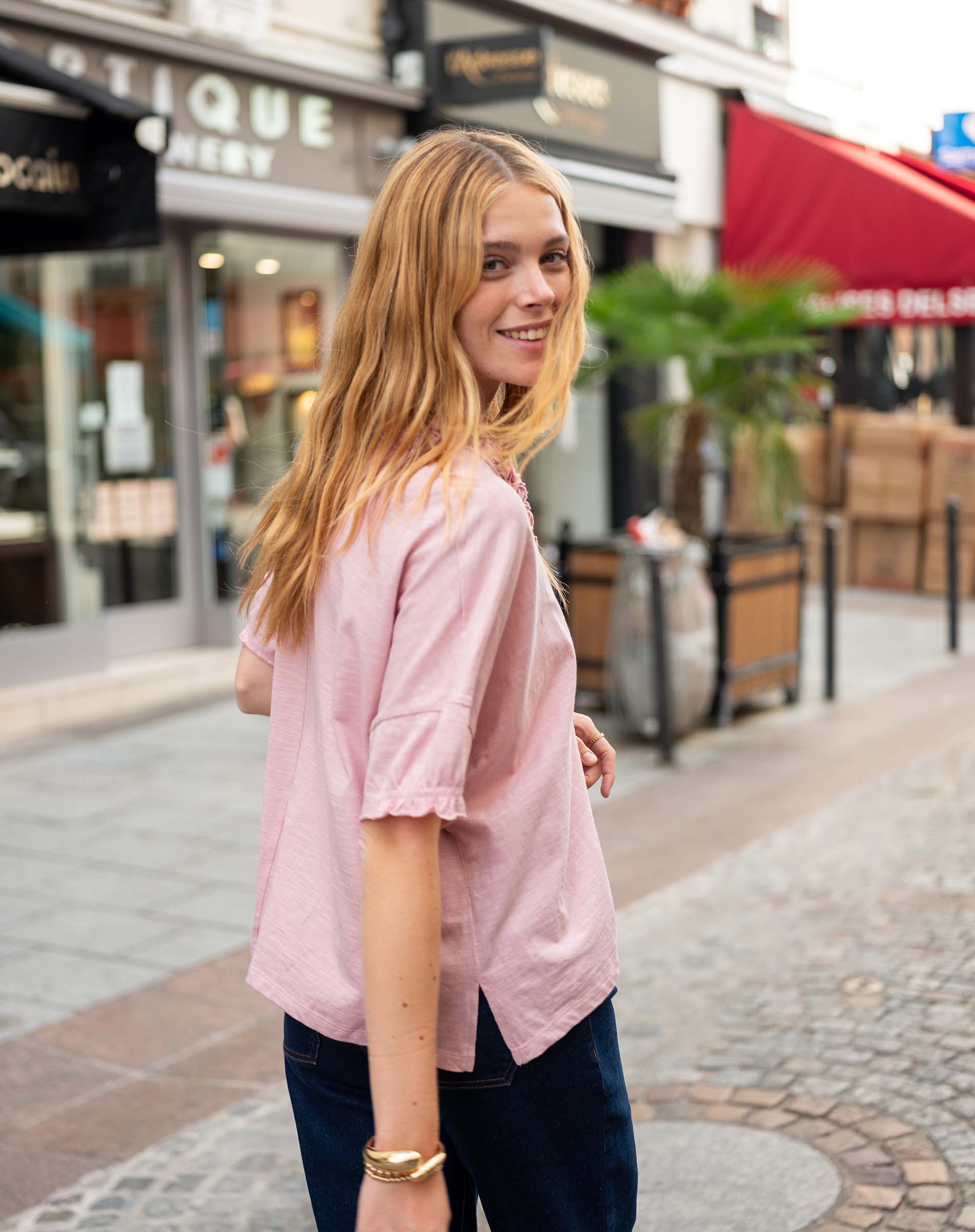 Woman in a pink shirt standing on a street with shops in the background