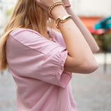 Person wearing a pink shirt with rolled-up sleeves and gold bracelets on a blurred background