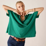 Woman wearing a green oversized shirt and blue jeans against a plain background