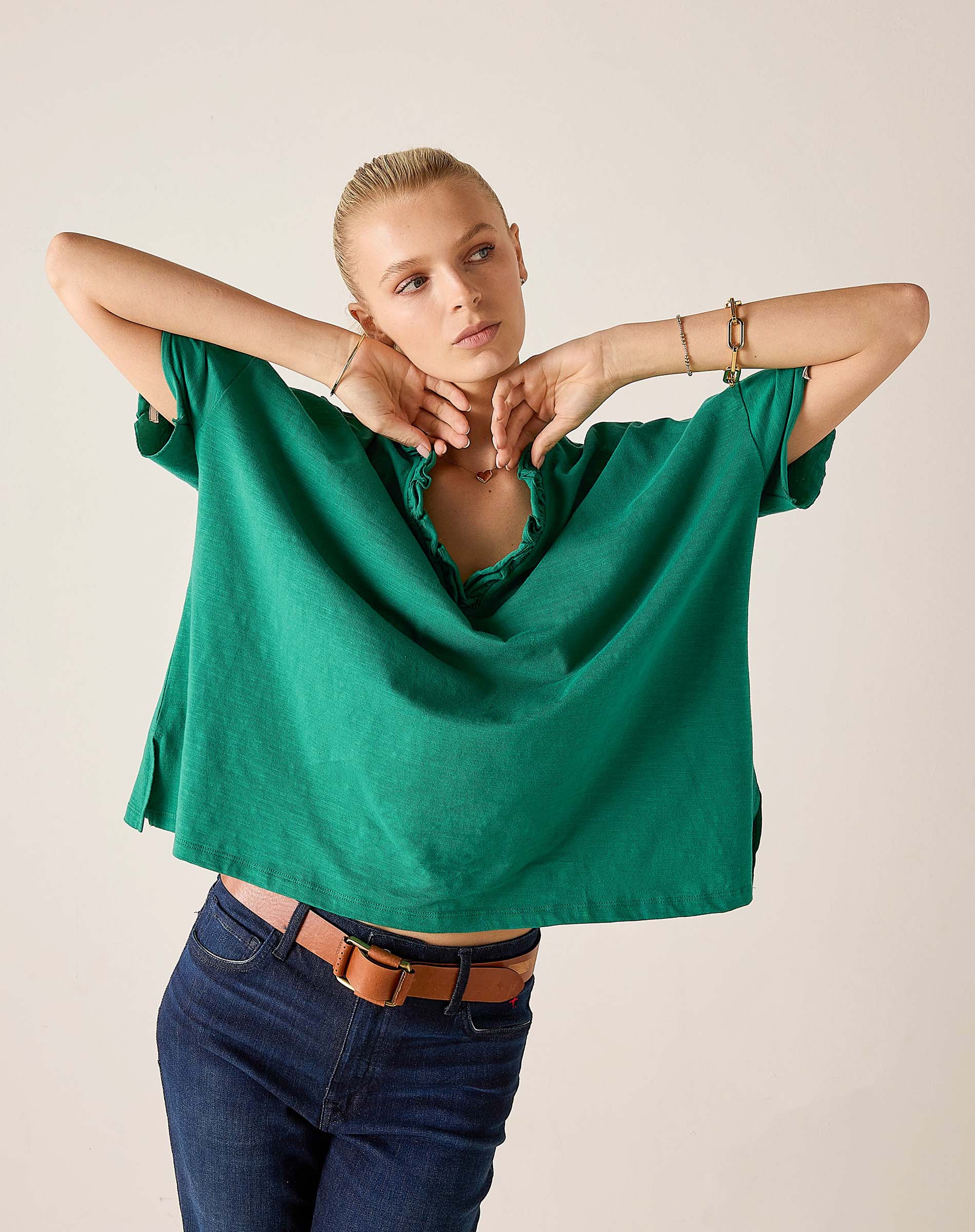Woman wearing a green oversized shirt and blue jeans against a plain background
