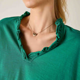 Close-up of a person wearing a green top with ruffled neckline and a gold necklace.