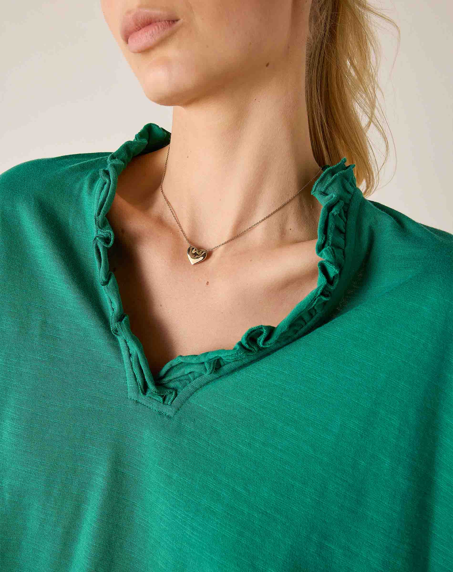 Close-up of a person wearing a green top with ruffled neckline and a gold necklace.