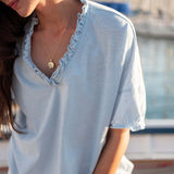 Woman wearing a light blue blouse with ruffled details, standing outdoors.
