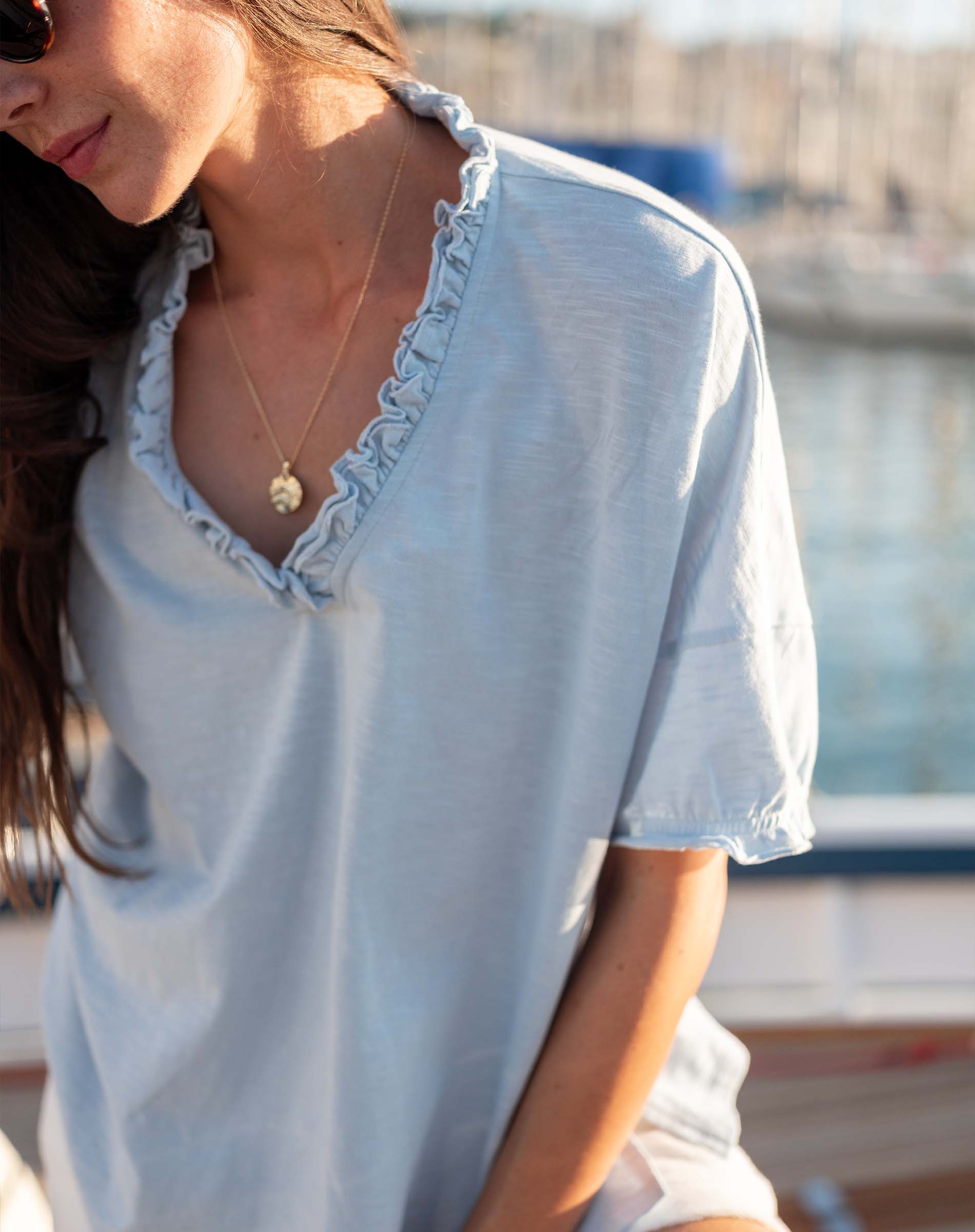 Woman wearing a light blue blouse with ruffled details, standing outdoors.