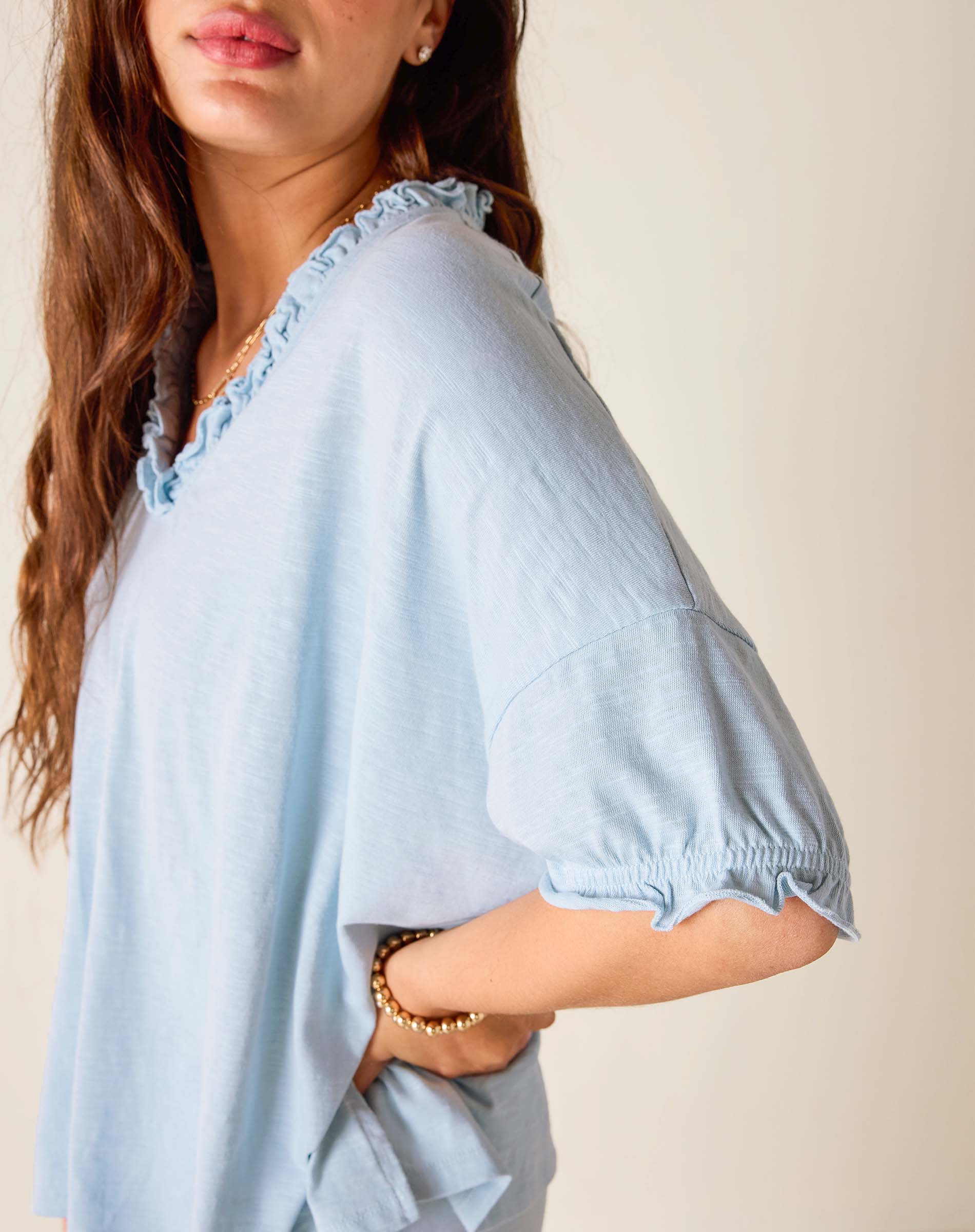 Light blue blouse with ruffled details worn by a person against a neutral background