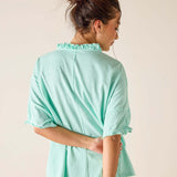 Woman wearing a light green blouse with ruffled collar against a plain background