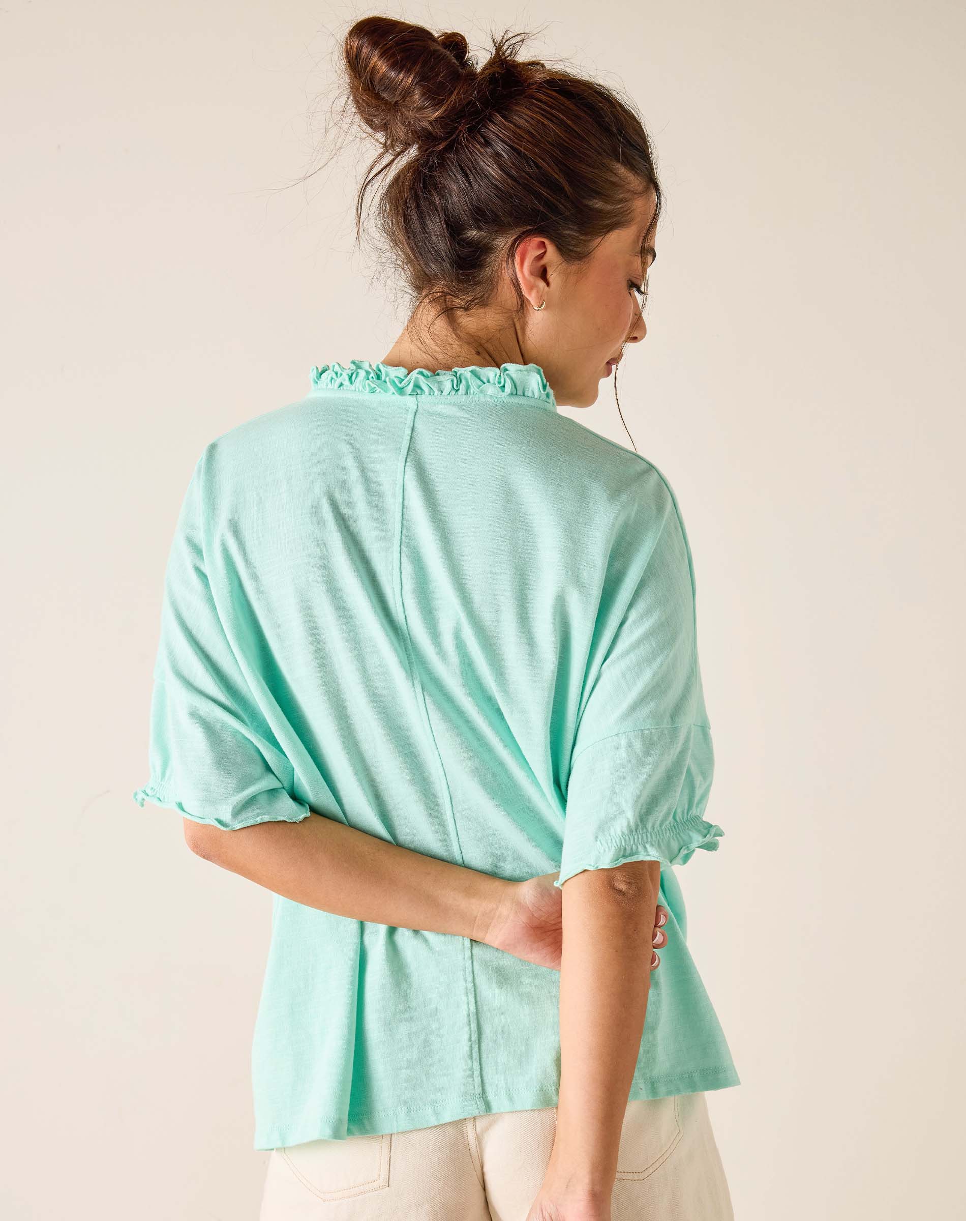 Woman wearing a light green blouse with ruffled collar against a plain background