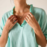 Person wearing a light blue top with ruffled trim, adjusting the neckline.