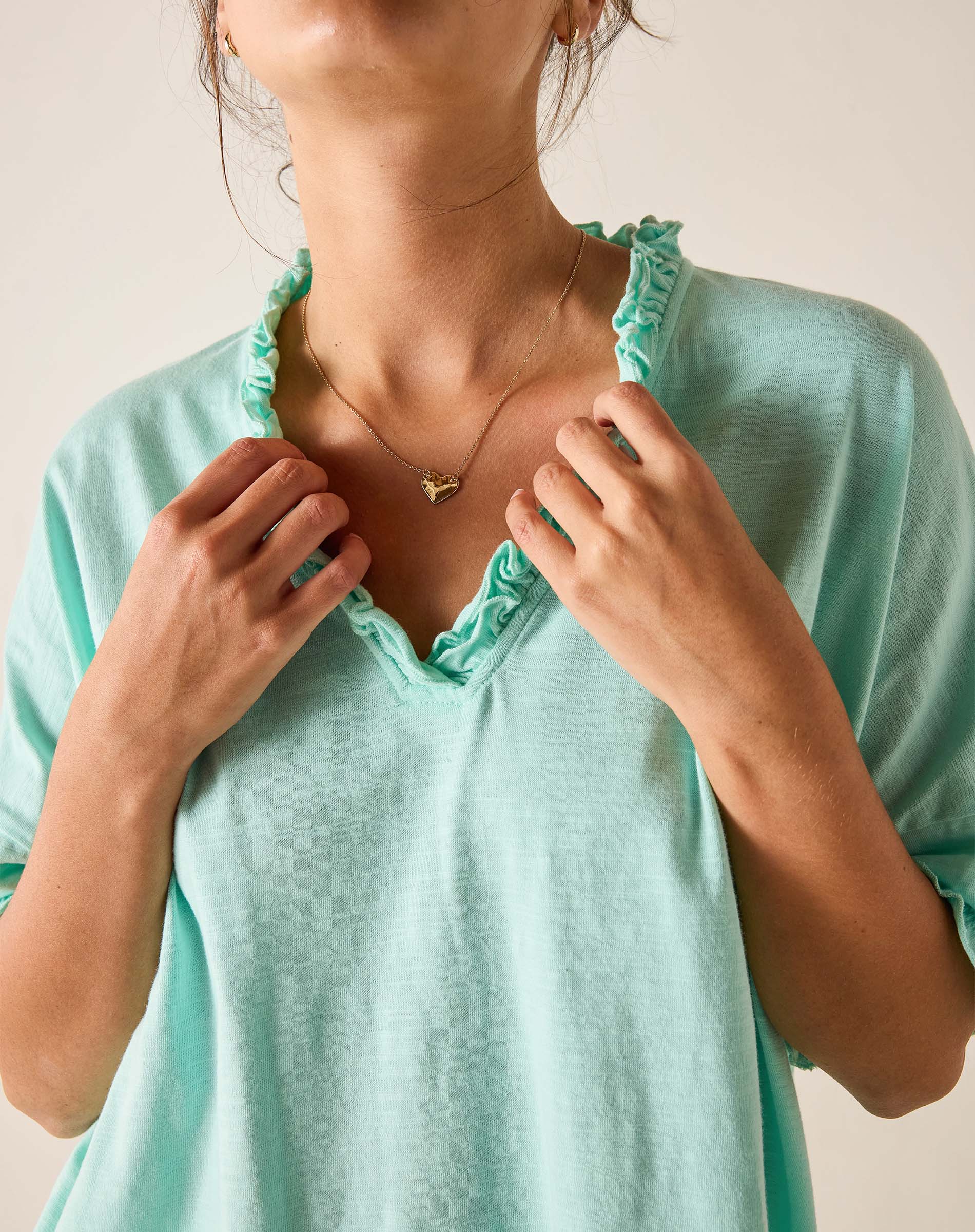 Person wearing a light blue top with ruffled trim, adjusting the neckline.
