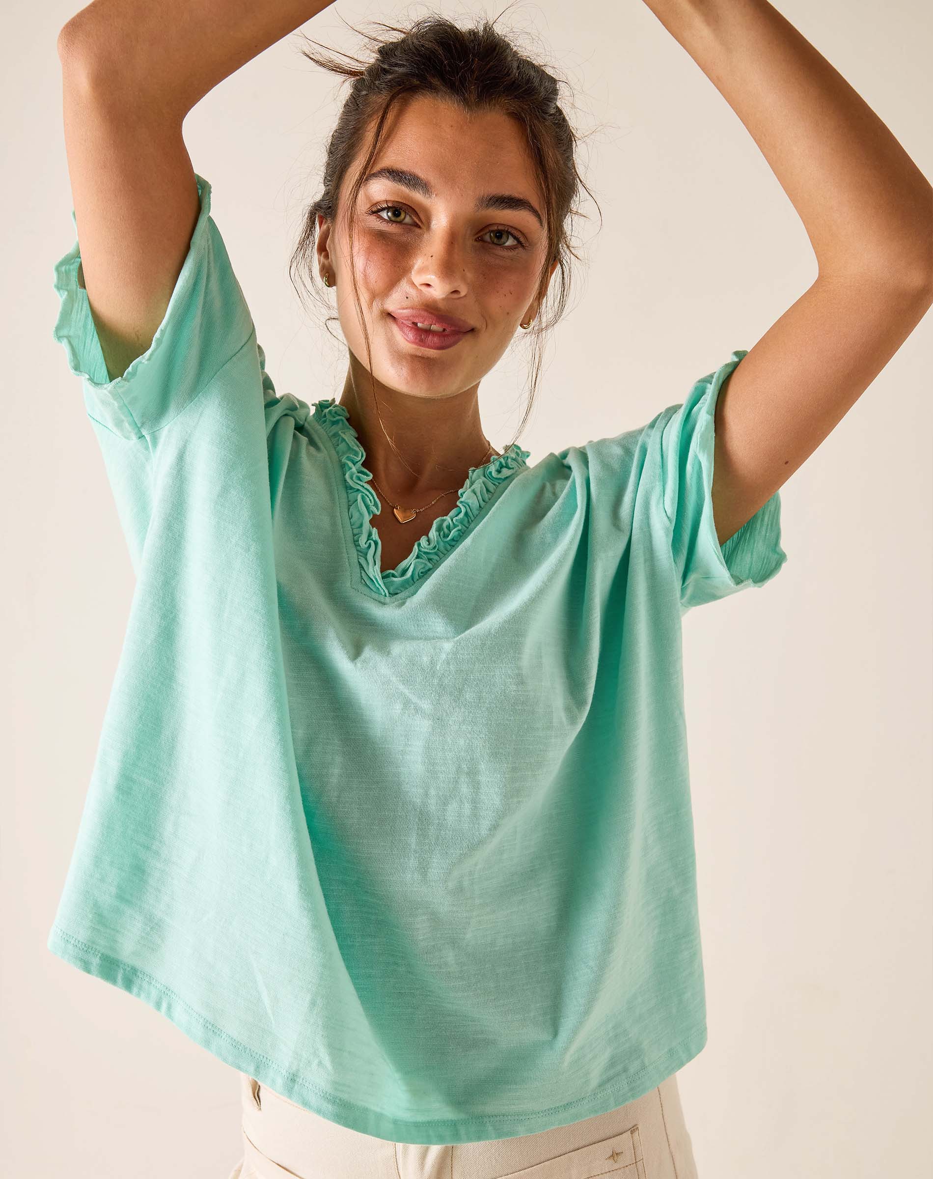 Woman wearing a light green blouse with ruffled neckline against a plain background