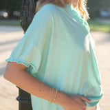 Person wearing a light blue top with ruffled sleeves in an outdoor setting