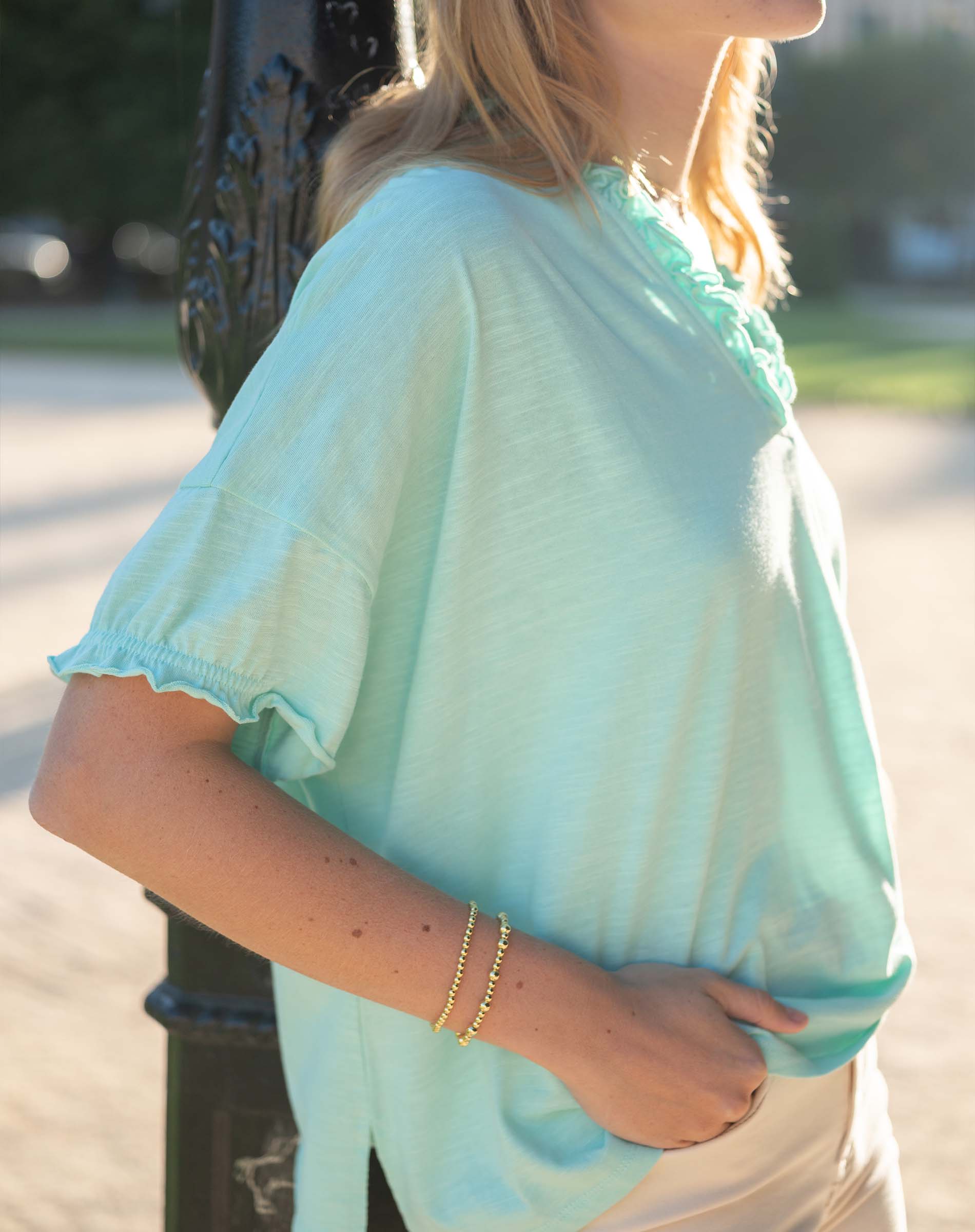 Person wearing a light blue top with ruffled sleeves in an outdoor setting