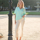 Woman in light blue shirt and white pants standing next to a lamp post in an outdoor setting.