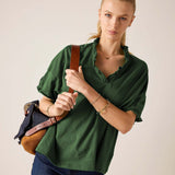 Model in a pine green ruffle tee with short sleeves and ruffled neckline, paired with dark wash denim jeans.