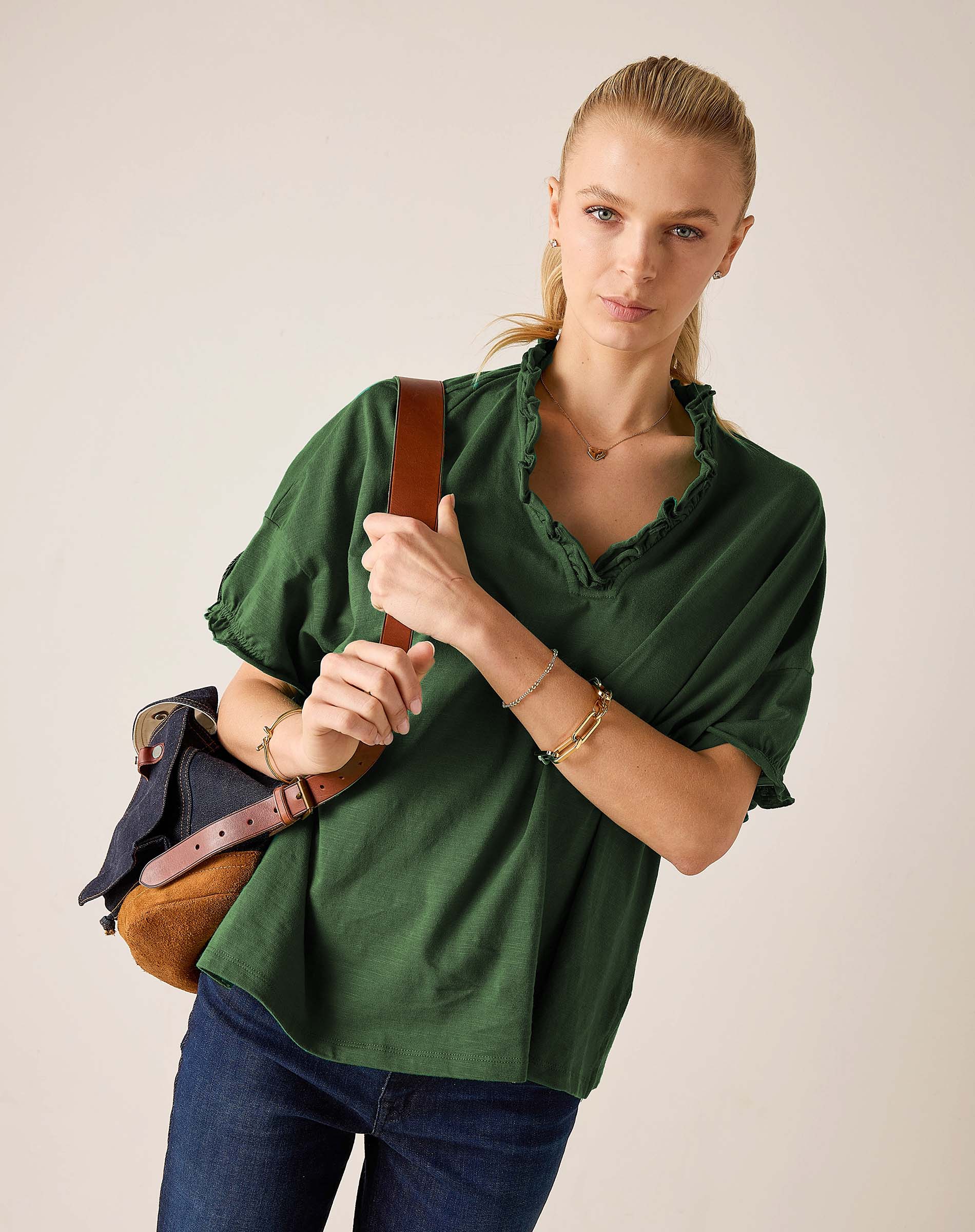 Model in a pine green ruffle tee with short sleeves and ruffled neckline, paired with dark wash denim jeans.