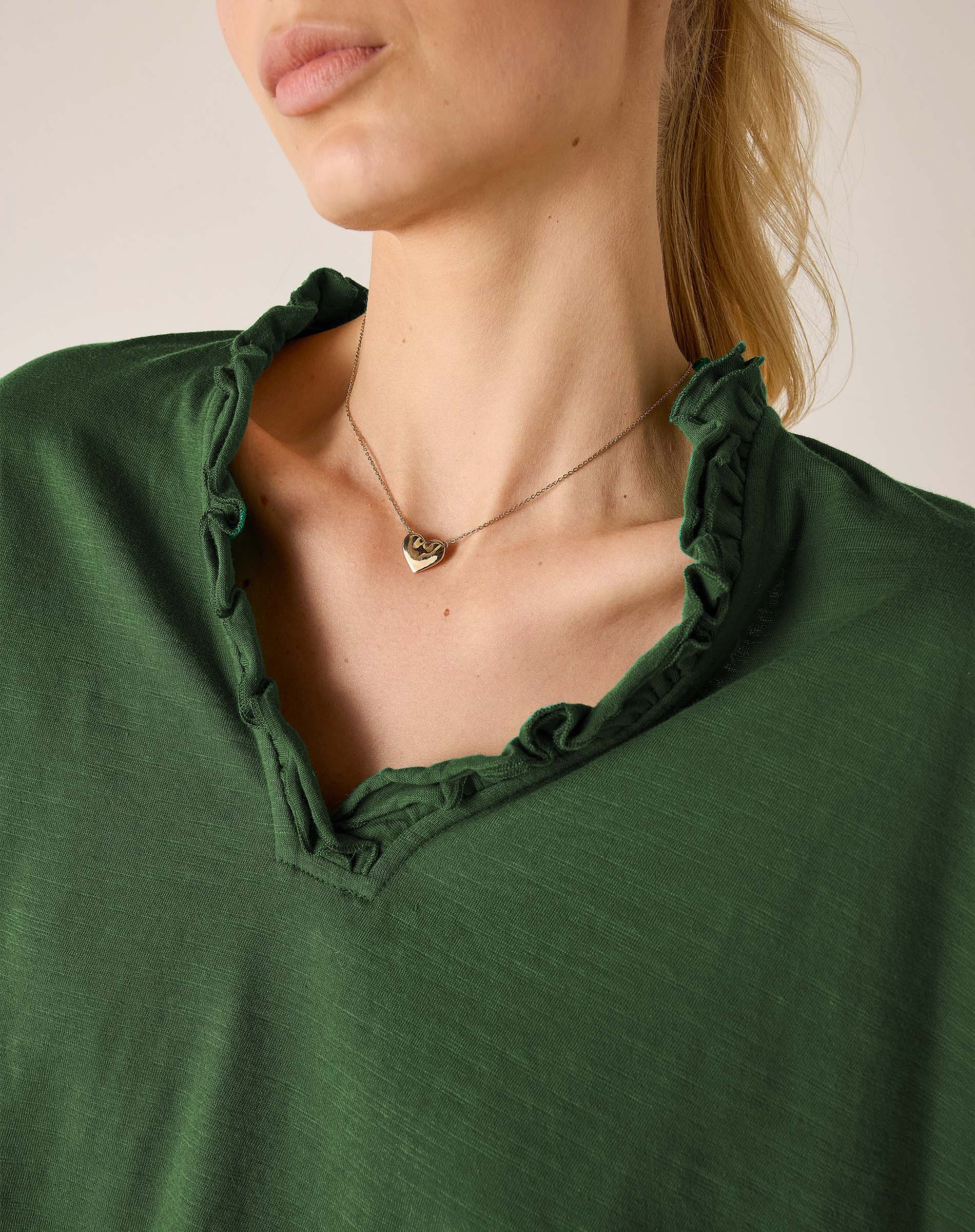 Model wearing a pine green ruffle tee with a scoop neckline and soft, draped fabric texture.