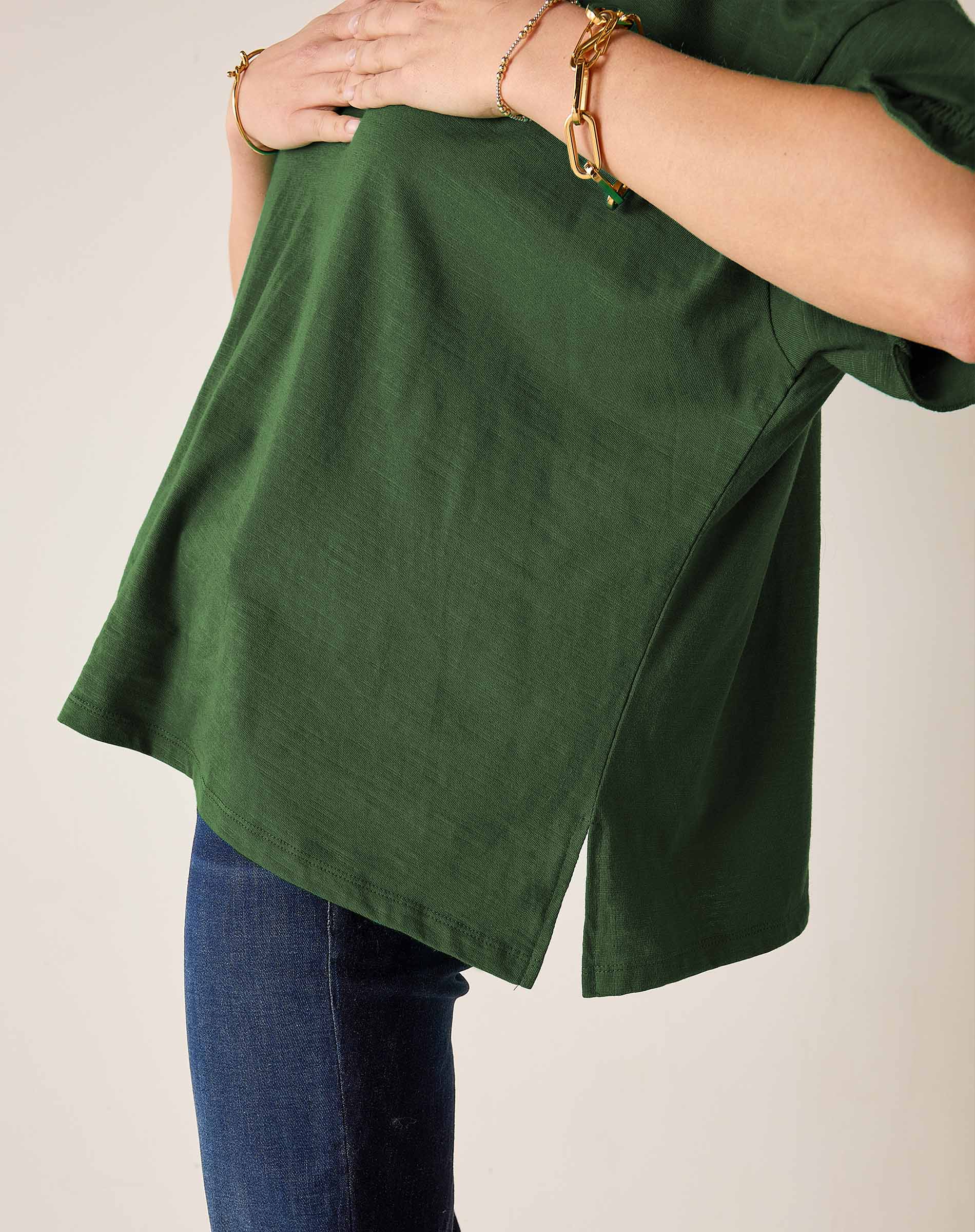 Model wearing an oversized pine green ruffle tee in a textured fabric, paired with blue denim jeans.