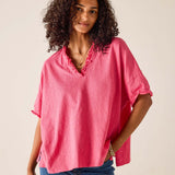 Woman wearing a pink blouse with rolled-up sleeves against a beige background