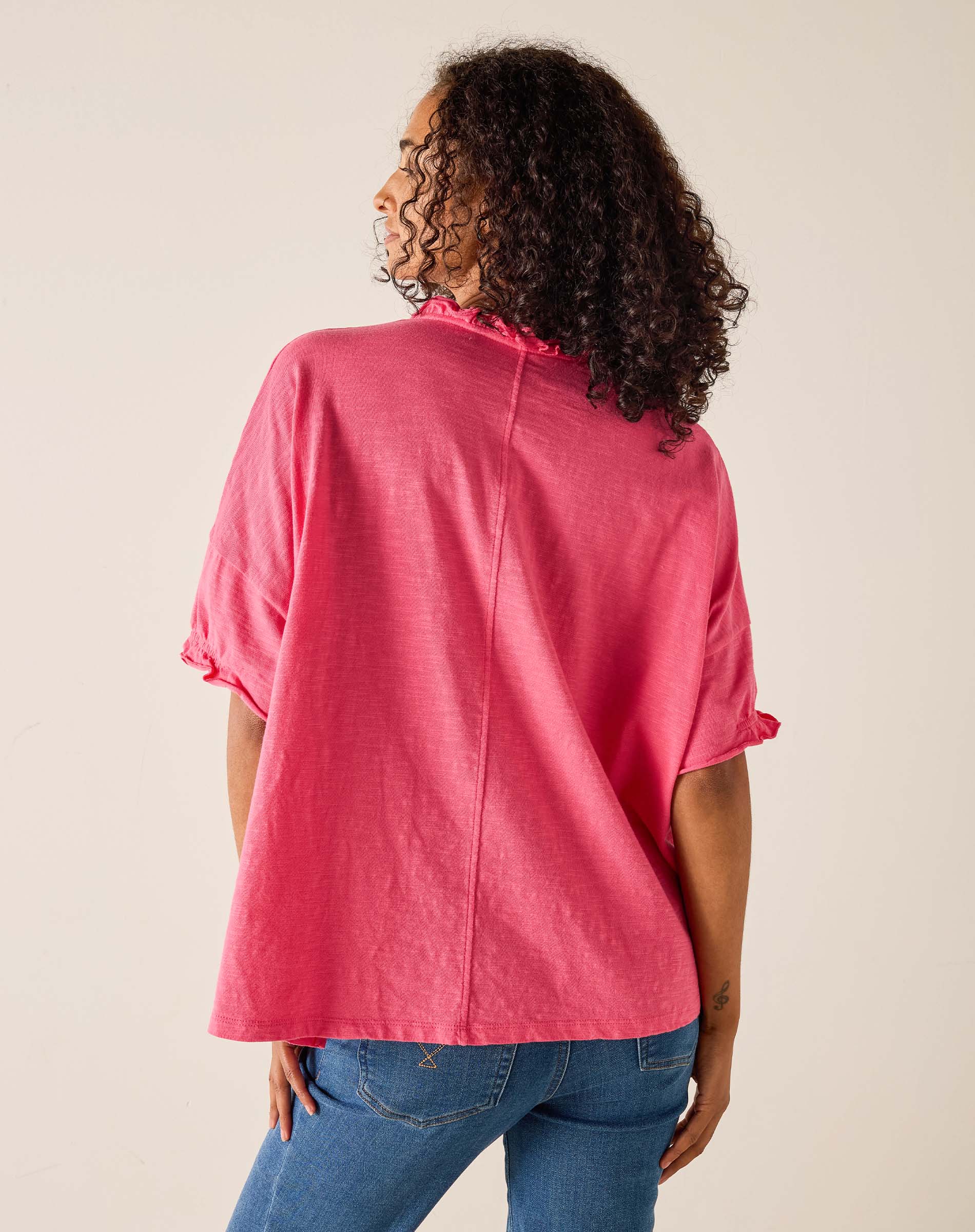 Person wearing a pink shirt and blue jeans on a beige background