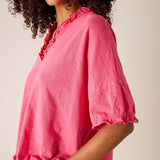Woman wearing a pink blouse with ruffled neckline against a neutral background