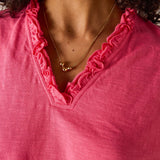 Close-up of a person wearing a pink top with ruffled neckline and a necklace.