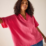 Woman wearing a pink blouse with ruffled neckline and blue jeans against a plain background