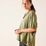 Woman wearing a green blouse with embellishments on a plain background