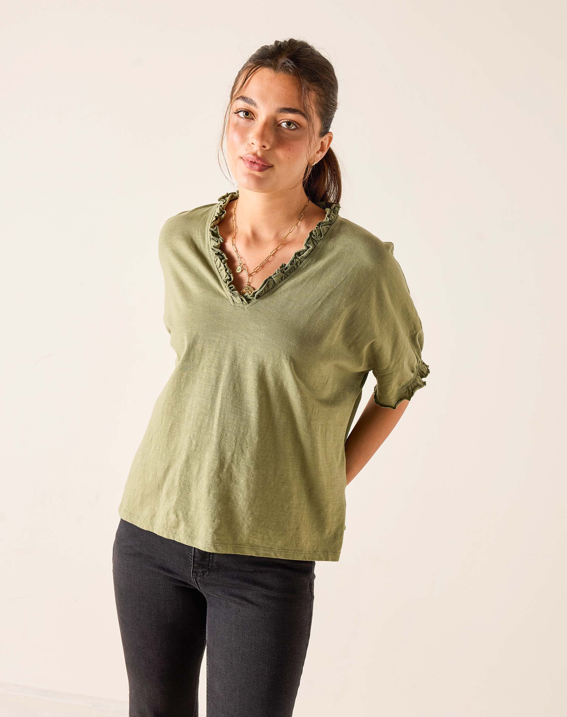 Woman wearing a green blouse with ruffled details on a plain background